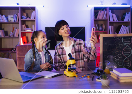 Caucasian mother with daughter sitting at table and having online video chat. 113203765