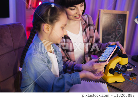 Caucasian mother and daughter using microscope for studying plant cells. 113203892