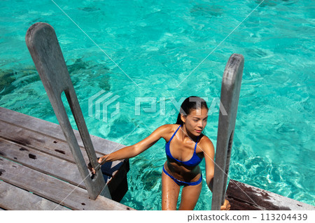 Beach travel vacation luxury woman in hotel villa swimming from ocean deck wearing bikini. This image is completely unretouched and unedited and model is with no makeup. Original Raw Image. Beach travel vacation luxury woman in hotel villa swimming from ocean deck wearing bikini. This image is completely unretouched and unedited and model is with no makeup. Original Raw Image. 113204439