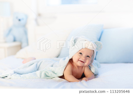 Baby boy in blue towel on white bed 113205646
