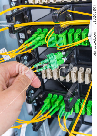 Hand of computer technician connecting fiber optics cable into data switch 113205807