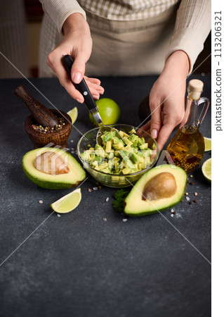 Woman mixing Sliced chopped avocado fruit with lime juice and species in a glass bowl at domestic kitchen Woman mixing Sliced chopped avocado fruit with lime juice and species in a glass bowl at domestic kitchen 113206321