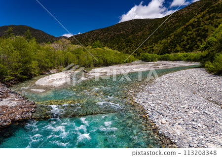 Fast flowing clear river running through a forest and mountains 113208348