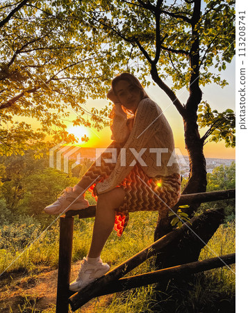 Urban sunset solace: woman on fence, embracing cityscape view Urban sunset solace: woman on fence, embracing cityscape view 113208741