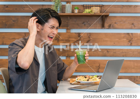 A young Asian man looking at a computer while eating at a cafe (flame/trouble/troubled/surprised/mistake/failure) 113208830