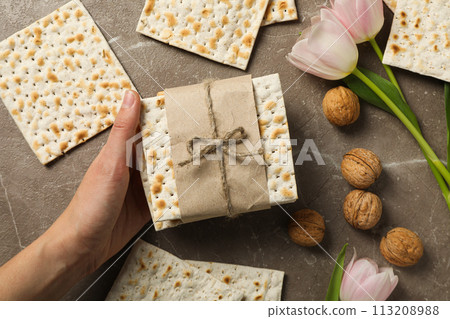Matzo in hand, nuts and flowers on gray background, top view 113208988