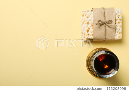 Cup of wine and matzo on light yellow background, space for text 113208996