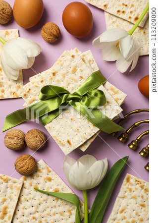 Matzo, eggs, nuts, flowers and hanukkiah on purple background, top view 113209000