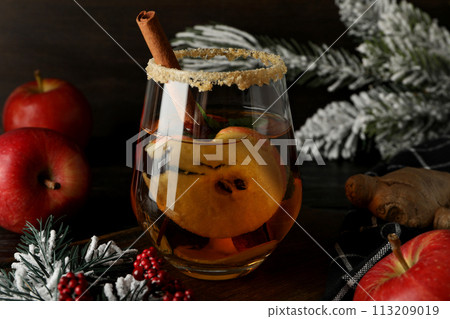 Glass with cider, apples and branches of christmas tree on dark wooden background, close up 113209019