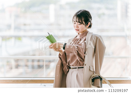 A businesswoman/young woman checking the time on her watch while looking at her schedule book 113209197