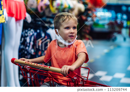 Boy sitting in shopping cart clothing store hypermarket, interested curious emotion, happy childhood 113209744