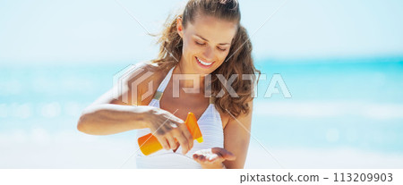 Happy young woman on beach applying sun screen creme 113209903