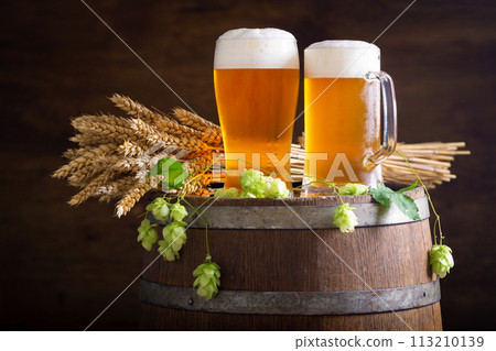 Glasses of beer, wheat ears and green hops on wooden barrel Glasses of beer, wheat ears and green hops on wooden barrel 113210139