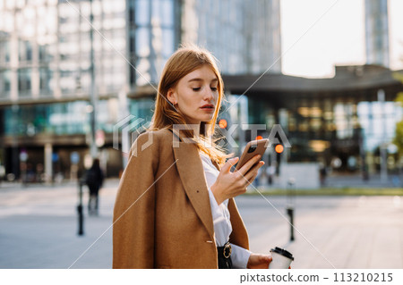 Young smiling business woman in jacket with coffee cup using mobile phone Young smiling business woman in jacket with coffee cup using mobile phone 113210215