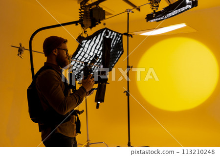 Man capturing large yellow background with camera at film studio. 113210248