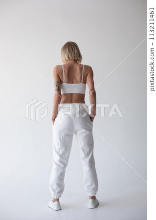 Beautiful blonde girl in a white top and tights posing on a white background. Posing with his back. 113211461