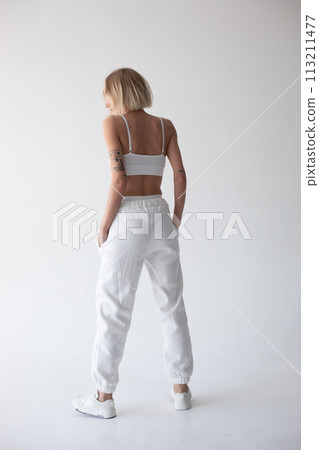 Beautiful blonde girl in a white top and tights posing on a white background. Posing with his back. Beautiful blonde girl in a white top and tights posing on a white background. Posing with his back. 113211477