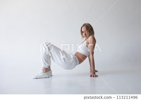 Beautiful blonde girl in a white top and tights posing on a white background Beautiful blonde girl in a white top and tights posing on a white background 113211496