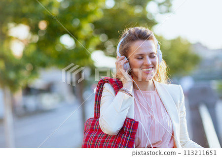 happy stylish woman in city listening to music with headphones 113211651