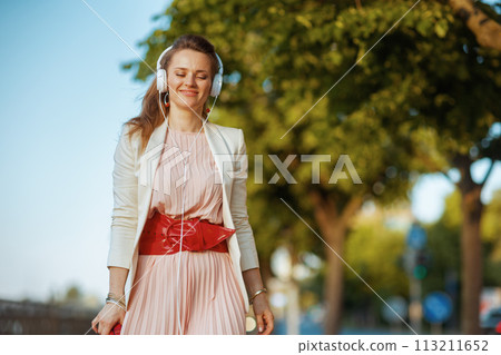 elegant woman in pink dress and white jacket in city walking elegant woman in pink dress and white jacket in city walking 113211652