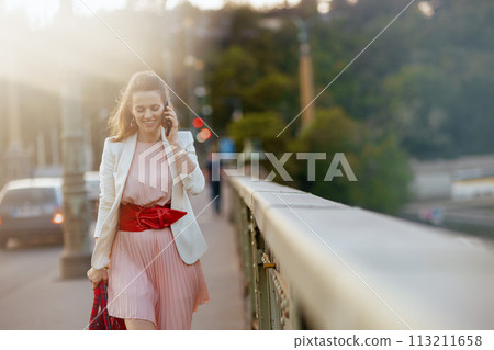 smiling stylish woman in dress and jacket in city using phone 113211658