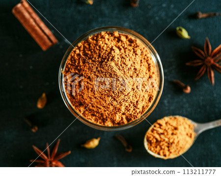 Indian or pakistani masala powder in spoon and small glass bowl. Close up view of homemade dry curry garam masala mix spices blend on dark background. Indian or pakistani masala powder in spoon and small glass bowl. Close up view of homemade dry curry garam masala mix spices blend on dark background. 113211777
