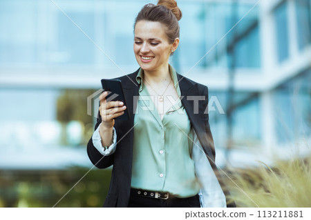 happy woman worker near office building using phone and walking 113211881