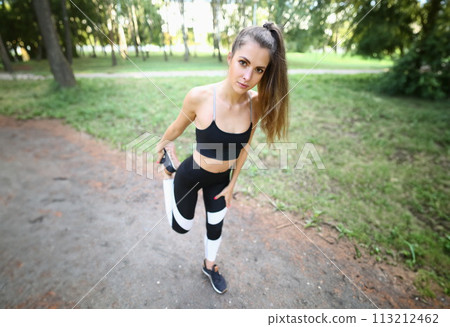 Girl in sportswear stretches leg muscles in park. 113212462