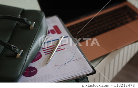 Clipboard documents and ballpoint pen lying on open green laptop bag closeup 113212478