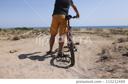 Man holding bike on sand near sea closeup 113212489