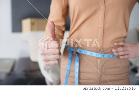 Woman with measuring tape at her waist showing thumb up closeup 113212516