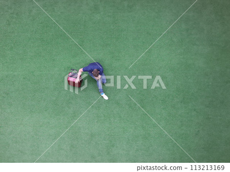 Sad man with suitcase sitting on green grass and holding his head top view 113213169