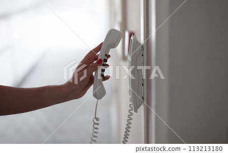 Woman hand picking up phone in hotel corridor closeup Woman hand picking up phone in hotel corridor closeup 113213180