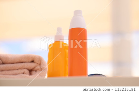 Two orange bottles with sunscreen lying on beach near towels closeup Two orange bottles with sunscreen lying on beach near towels closeup 113213181