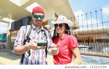 Young man and woman in sunglasses standing on platform of train and looking at screen of mobile phone Young man and woman in sunglasses standing on platform of train and looking at screen of mobile phone 113213194