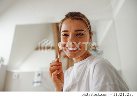 Beautiful woman use jade roller to massage her face standing in bathroom. Spa self beauty procedure Beautiful woman use jade roller to massage her face standing in bathroom. Spa self beauty procedure 113213253