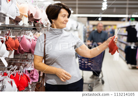 Mature woman carefully choosing bra in clothes department hypermarket Mature woman carefully choosing bra in clothes department hypermarket 113214105