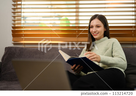 Relaxed young caucasian woman sitting on sofa at home and reading book Relaxed young caucasian woman sitting on sofa at home and reading book 113214720