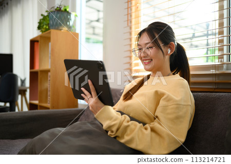 Smiling young woman in eyeglasses watching video on digital tablet at home Smiling young woman in eyeglasses watching video on digital tablet at home 113214721