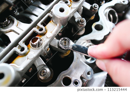 Car mechanic checking and adjusting valves of car engine with a ring wrench 113215444