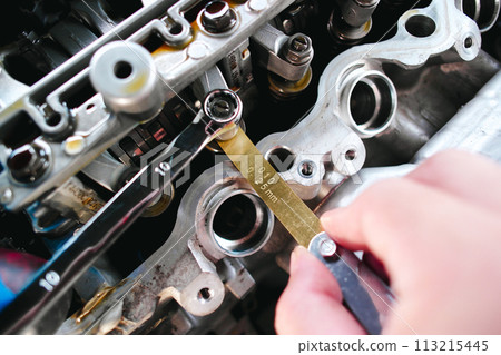Car mechanic checking and adjusting valves of car engine with feeler gauge or thickness gauge tool Car mechanic checking and adjusting valves of car engine with feeler gauge or thickness gauge tool 113215445