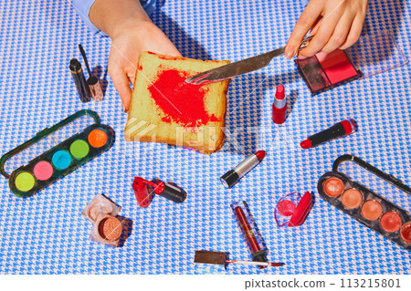 Promotional image of organic cosmetics products. Woman putting lipstick on toast bread against blue tablecloth. Promotional image of organic cosmetics products. Woman putting lipstick on toast bread against blue tablecloth. 113215801