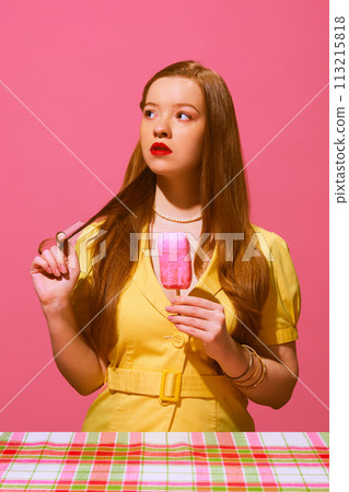 Portrait of redhead young woman with red lips, in yellow dress standing with ice cream and thoughtful face against pink background Portrait of redhead young woman with red lips, in yellow dress standing with ice cream and thoughtful face against pink background 113215818