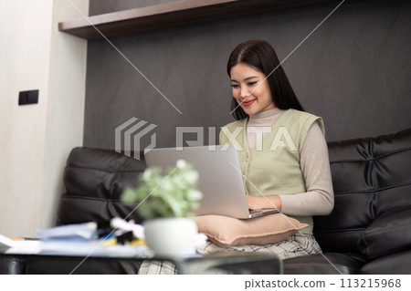 Happy young asian freelance business woman sitting on the sofa at home working on laptop computer 113215968