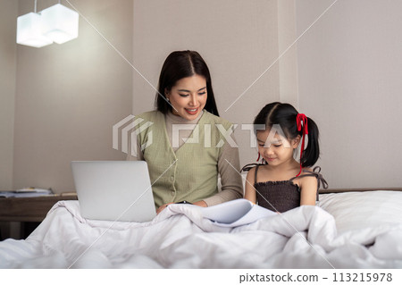 Mom work from home with children. Mother working on bed laptop in bedroom with child daughter. Funny authentic lifestyle family moment 113215978