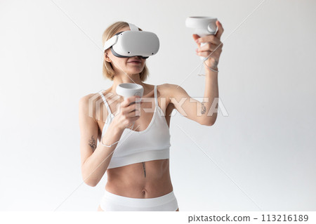 Beautiful thin girl in white shorts and a top in a virtual reality helmet posing on a white background Beautiful thin girl in white shorts and a top in a virtual reality helmet posing on a white background 113216189