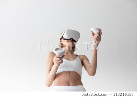 Beautiful thin girl in white shorts and a top in a virtual reality helmet posing on a white background Beautiful thin girl in white shorts and a top in a virtual reality helmet posing on a white background 113216195