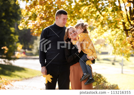 Family day. Young dad, mom holds adorable little child daughter in hands enjoying spend time together at weekend outdoor at autumn park, kid kisses mommy. Parental love, mental health. Happy childhood 113216355