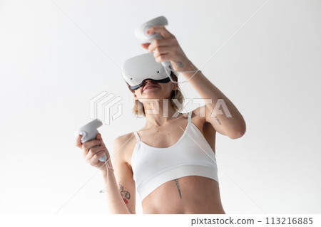 Beautiful thin girl in white shorts and a top in a virtual reality helmet posing on a white background Beautiful thin girl in white shorts and a top in a virtual reality helmet posing on a white background 113216885