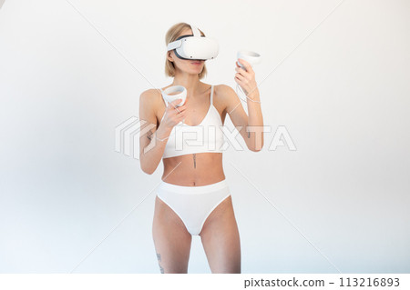 Beautiful thin girl in white shorts and a top in a virtual reality helmet posing on a white background Beautiful thin girl in white shorts and a top in a virtual reality helmet posing on a white background 113216893